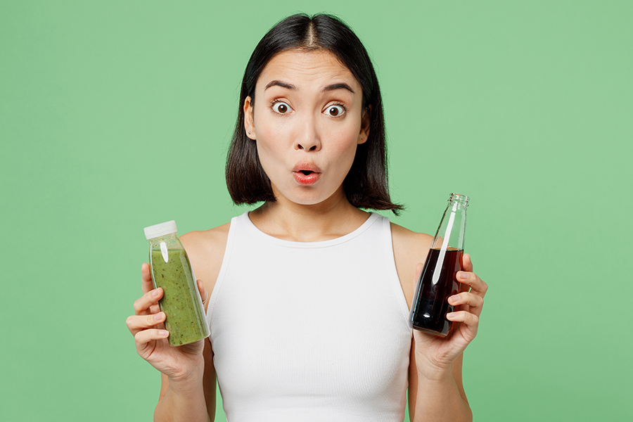 Mujer joven sujetando un refresco oscuro y un jugo verde